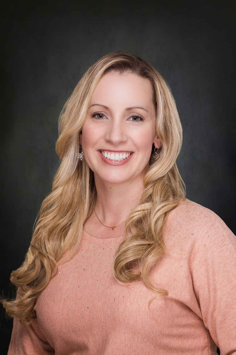 A smiling woman with blonde hair poses against a dark backdrop for a corporate headshot photographer Vermont session.