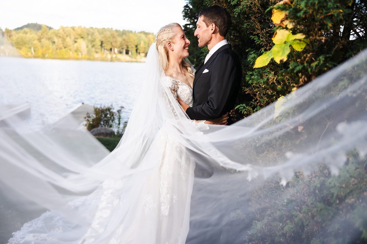 A bride and groom embrace by a lake during a session with a professional photographer Vermont specialist.